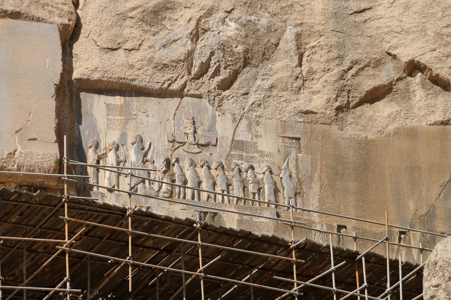 A cliff in Iran carved with a king, prisoners, and three columns of cuneiform writing.