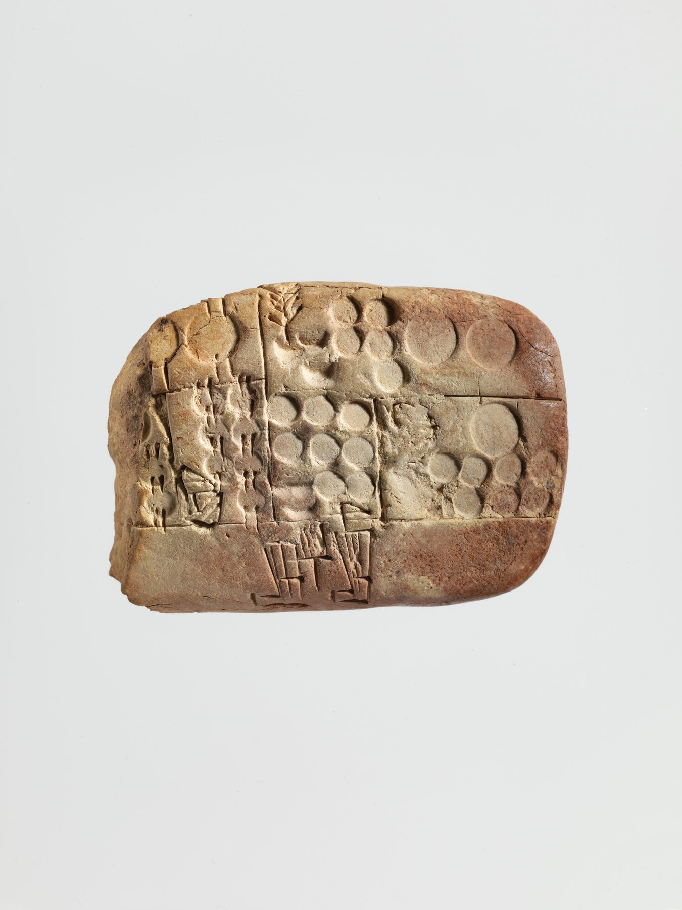 A baked clay tablet packed with small wedge-shaped marks, photographed so the dents look physical.